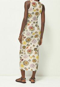 Robe midi fleurie avec une silhouette cintrée, présentant un fond crème et des motifs floraux multicolores. Portée avec des sandales à brides marron.