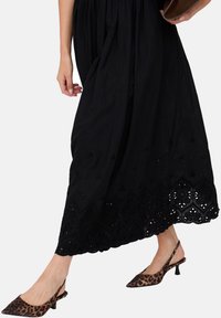 Schwarzes Maxikleid mit besticktem Saum und Schlitzen. Beige-braune Slingback-Pumps mit Leopardenmuster. Glatte Stoffstruktur mit fließendem Design.