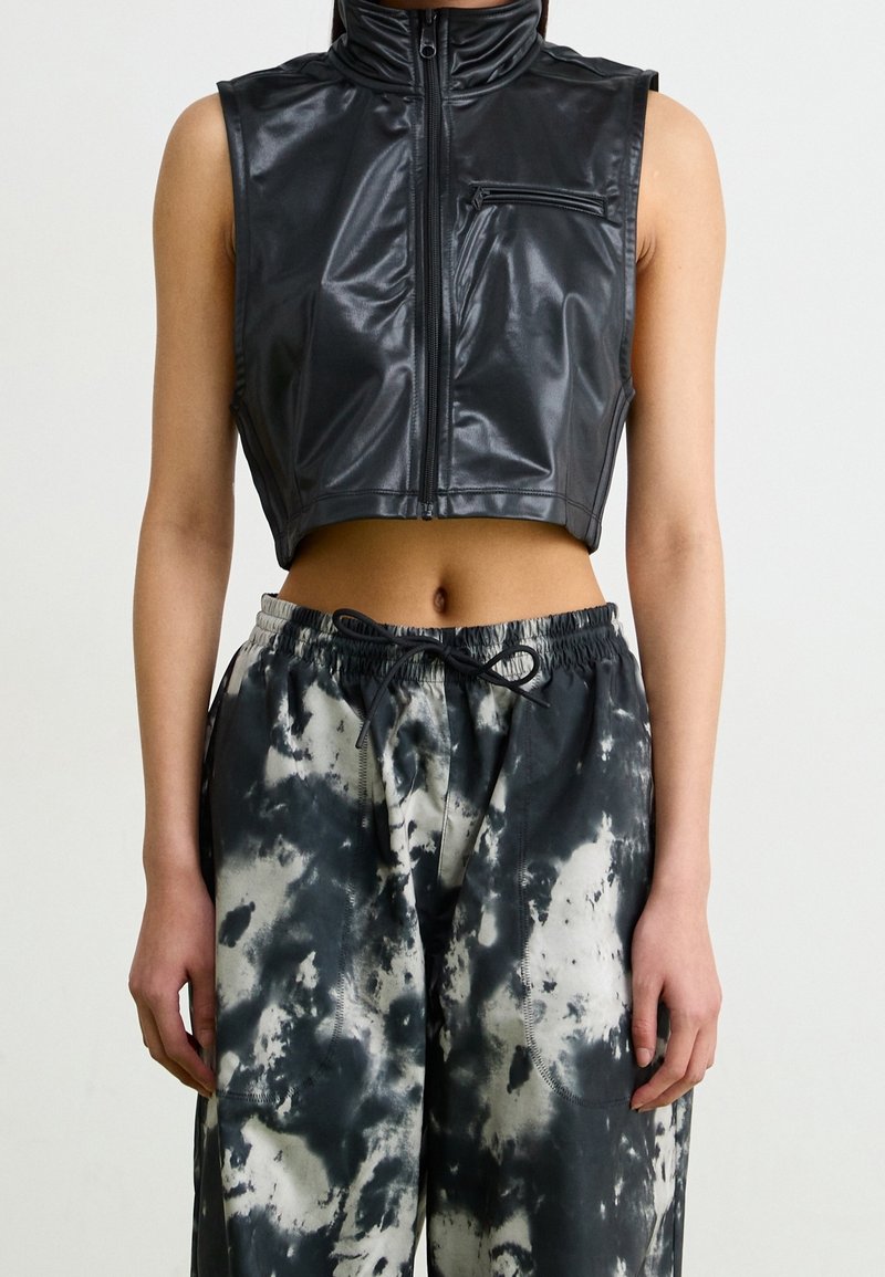 Veste courte noire en matériau brillant avec un col montant et une fermeture éclair avant. Associée à un pantalon ample à motif tie-dye gris et blanc.