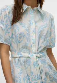 Abito camicia con bottoni in tessuto leggero, caratterizzato da una fantasia floreale blu. Ha maniche corte a palloncino e una cintura in vita per una vestibilità regolabile.