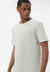 Camiseta de manga corta gris claro con cuello redondo, textura suave y diseño minimalista. Presenta un corte holgado y hombros sin costuras.