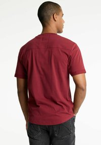 Bordeauxrotes T-Shirt mit kurzen Ärmeln und rundem Halsausschnitt. Verfügt über einen flachen Rückenpasse und einen aufgerollten Saum an den Ärmeln. Glatte Baumwolltextur.