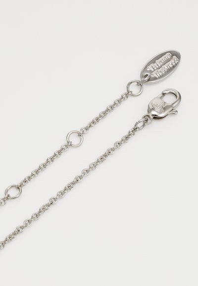 Sudraba ķēdes kaklarota ar ovālu piekariņu un omā zvanu, ar noapaļotām saites un gludu virsmu. Piekariņā iegravēts zīmols.