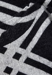 Czarna i biała dzianina z geometrycznym wzorem, ukazująca fałdy i szczegóły tekstury.