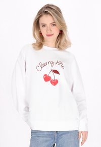 Sweatshirt bianco in cotone con stampa grafica di due ciliegie rosse e il testo "Cherry Me" in un carattere giocoso. Fit rilassato e polsini a coste.