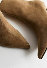 Bottines en daim marron avec un design à bout pointu, présentant une texture lisse et des coutures nettes le long des coutures.