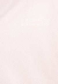Tissu blanc texturé avec un texte blanc légèrement en relief répétant "LACOSTE" en motif empilé près du centre.