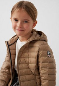 Beige donzen jas met capuchon, voorzien van een doorgestikt ontwerp, ritssluiting aan de voorkant en een logopatch op de linkermouw. Glad materiaal en lichte uitstraling.