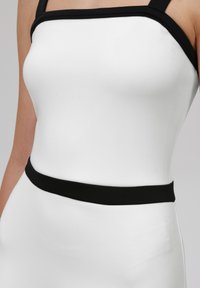 Hvit kjole med en tettsittende silhuett, med svarte stropper og svart midjebånd. Glatt tekstur og minimalistisk design.