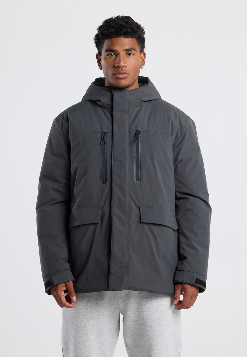 Dark gray insulated jacket with a hood, featuring two chest zip pockets, two front flap pockets, and elastic cuffs. Smooth texture, casual fit.