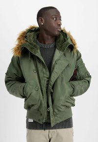 Grüne Pufferjacke mit Kapuze aus Kunstfell, ausgestattet mit Druckknöpfen, gerippten Bündchen und Seitentaschen. Texturiert, isoliert und mit modernem Schnitt.