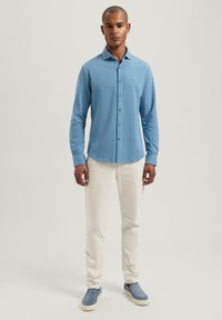 Camicia azzurro chiaro con colletto a punta, abbinata a pantaloni bianchi slim-fit e scarpe blu slip-on. Tessuto dalla texture liscia.