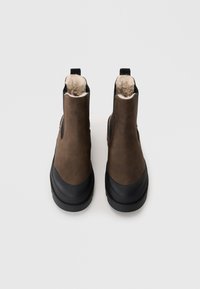 Bottines en cuir marron avec doublure pelucheuse, semelles en caoutchouc noir et panneaux latéraux élastiques. Comprend des languettes pour un enfilage facile.
