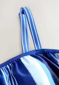 Tissu rayé bleu et bleu clair avec une texture lisse, présentant un design froncé et des bretelles ajustables. Détail en métal doré visible.