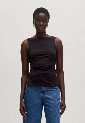 Schwarzes ärmelloses Oberteil mit einem runden Halsausschnitt, das ein gerafftes Design aufweist. Kombiniert mit hellblauen Jeans, die eine figurbetonte, aber entspannte Silhouette betonen.