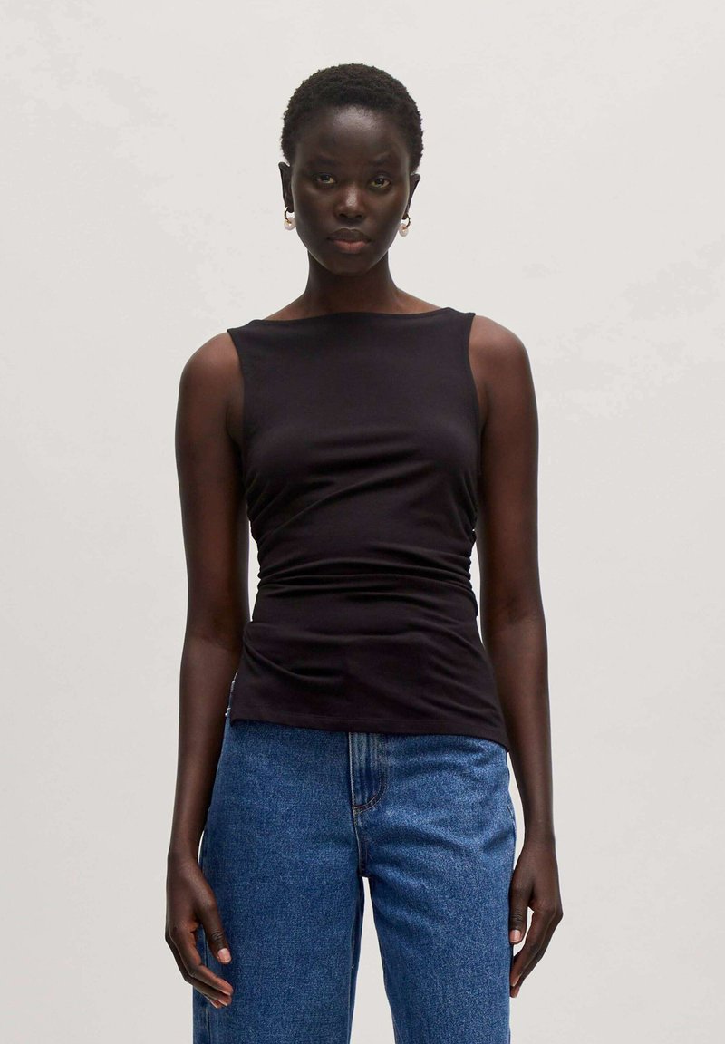 Schwarzes ärmelloses Oberteil mit einem runden Halsausschnitt, das ein gerafftes Design aufweist. Kombiniert mit hellblauen Jeans, die eine figurbetonte, aber entspannte Silhouette betonen.