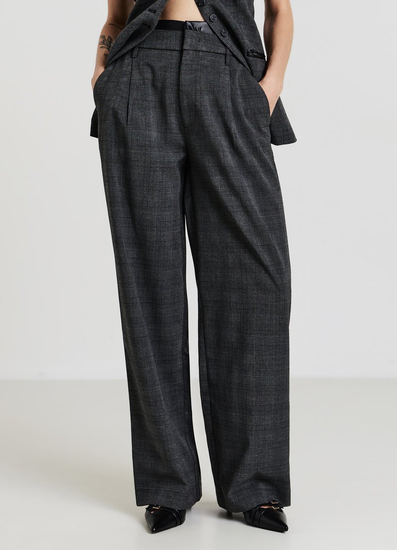 Grau karierte Hose mit weitem Bein, Falten und Seitentaschen. Hergestellt aus einem strukturierten Stoff. Kombiniert mit spitzen schwarzen Schuhen.