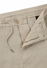 Pantaloni in lino beige con chiusura a bottone, zip e cordoncino. L'interno presenta una fodera a motivo discreto e una cerniera in metallo.