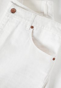 I pantaloni in denim bianco presentano un design classico con dettagli in ottone sulla patta e una tasca anteriore. La texture è liscia con un sottile motivo a righe.