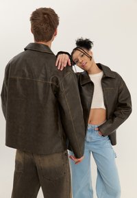 Barna bőrkabátok matt felülettel, gallérral és első zsebekkel, világoskék farmerrel és crop top felsővel párosítva.