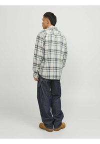 Kariertes Flanellhemd in Creme, Blau und Grau, mit lockerem Schnitt. Kombiniert mit dunklen Jeans und braunen Clogs.