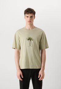 Lysegrøn bomulds t-shirt med et centreret grafisk motiv af et palmetræ, korte ærmer, rund hals og en afslappet pasform.