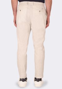 Pantaloni slim-fit beige chiaro con una sottile trama, due tasche posteriori e dettagli con bottoni, abbinati a sneakers bianche.