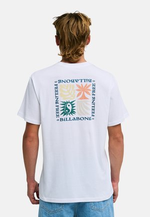 Mężczyzna noszący białą koszulkę Billabong z kolorowymi abstrakcyjnymi wzorami roślin i słońca oraz napisem „FEELING FREE” na plecach, w połączeniu z niebieskimi dżinsami.