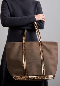 Bruine tote bag met gestructureerde gouden strepen; gemaakt van duurzaam fabric, heeft een brede body en lange handvatten voor gemakkelijk dragen.