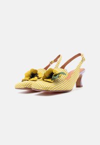 Κίτρινα παπούτσια slingback με λευκές πουά, διακοσμημένα με μεγάλα υφασμάτινα λουλούδια στο μύτο και μικρό τακούνι kitten με δερμάτινο λουράκι σε ταν απόχρωση.