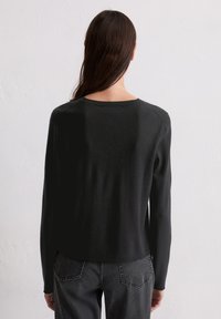 Pull noir à manches longues avec un col rond et des poignets côtelés. Texture douce et coupe décontractée, associé à un jean gris vu de dos.