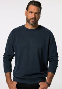 Felpa girocollo blu navy realizzata in tessuto morbido, con maniche lunghe, polsini a coste e una piccola tasca decorativa sul braccio sinistro.