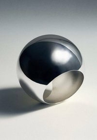 Bague en métal argenté hautement poli avec une large bande et un grand design courbé ouvert sur un fond neutre.