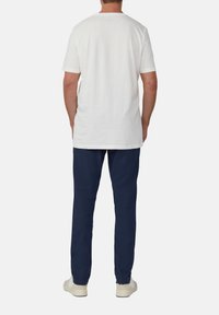 Witte katoenen T-shirt met korte mouwen, gecombineerd met donkerblauwe broek. De outfit heeft een relaxte pasvorm en een eenvoudig ontwerp, geschikt voor casual draag.