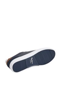 Kék sportcipő struktúrált felsőrésszel, fehér gumitalppal, amely halszálka mintás, és barna bőr díszítéssel a saroknál.