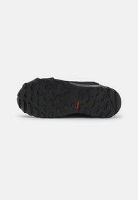 Suela de zapato negro para exteriores con un fuerte y texturizado dibujo de goma para agarre, con un mínimo acento rojo y un diseño contorneado.