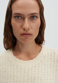 Cremefarbener Strickpullover mit einem strukturierten Muster, versehen mit einem rundem Ausschnitt und sichtbaren Rippen an den Rändern.