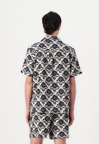 Σετ κον�τομάνικου πουκάμισου με κουμπιά και σορτς σε κρέμα χρώμα με ναυτικό λουλουδάτο ντεκόρ, με χαλαρή εφαρμογή και γιακά.