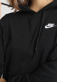 Svart Nike-hoodie med framficka, dragsko i huvan och vitt märke på bröstet. Mjukt tyg och avslappnad passform.