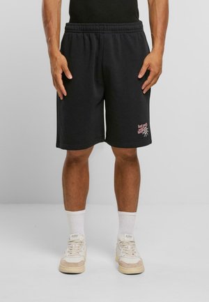 Shorts en coton noir avec une taille élastique, ornés d'un design graphique en texte rose sur la jambe gauche et d'une coupe décontractée.