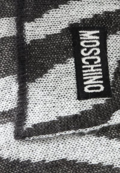 Tissu tricoté flou noir et blanc avec une étiquette rectangulaire noire affichant le texte blanc Moschino en lettres grasses.