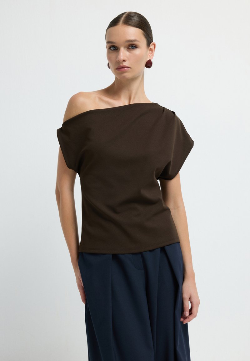 Top marrone senza spalle realizzato in tessuto liscio, con maniche ampie e una vestibilità rilassata, abbinato a pantaloni a palazzo blu navy.