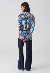 Camicia a maniche lunghe con un motivo geometrico blu e nero, caratterizzata da strisce audaci e forme varie. Abbinata a pantaloni flare in denim scuro.