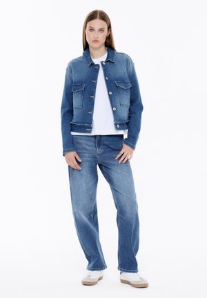 Denim jacket in light blue with two chest pockets, front-button fastening, and raw hem. Paired with matching loose-fitting jeans.