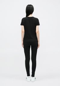 Fekete pamut rövid ujjú póló fekete, testhezálló leggingsszel párosítva. Az összeállítást finom márkajelzéssel ellátott fehér tornacipő teszi teljessé.