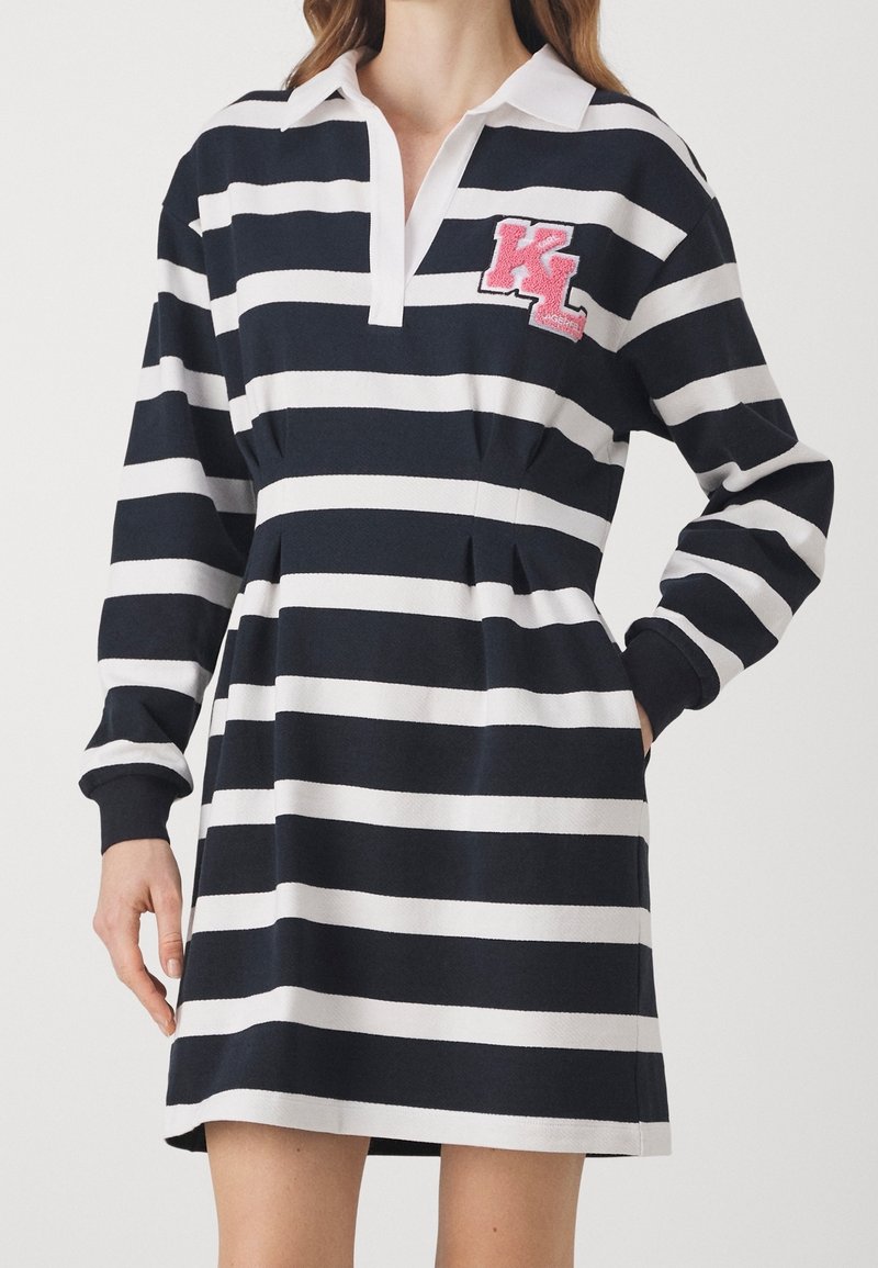 Randig klänning med marinblå och vita färger, polo-krage, långa ärmar och en rosa broderad "KL" logotyp på bröstet.