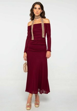 Vestido ajustado color marrón con diseño de hombros al descubierto, textura arrugada y una corbata de color marrón claro. Combinado con tacones de plataforma dorados y un bolso beige.