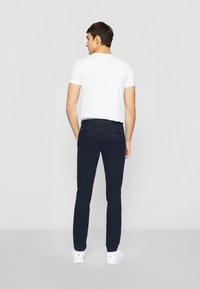 Tamno plave slim-fit chinos hlače od mješavine pamuka, s glatkom teksturom i klasičnim dizajnom s pet džepova. U kombinaciji s bijelom majicom i bijelim tenisicama.