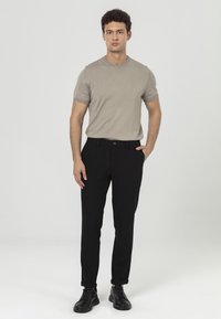 Lichtbeige shirt met korte mouwen van breiwerk, gecombineerd met zwarte op maat gemaakte broek en zwarte veterschoenen. Eenvoudig ontwerp, getailleerde silhouette en een gladde textuur.