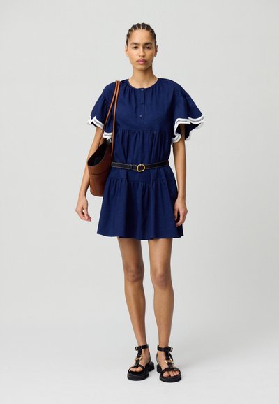 Vestido de lino azul marino con mangas cortas y con volantes, y borde de encaje. Presenta un escote abotonado, una cintura ajustada con un cinturón negro y una falda acampanada.